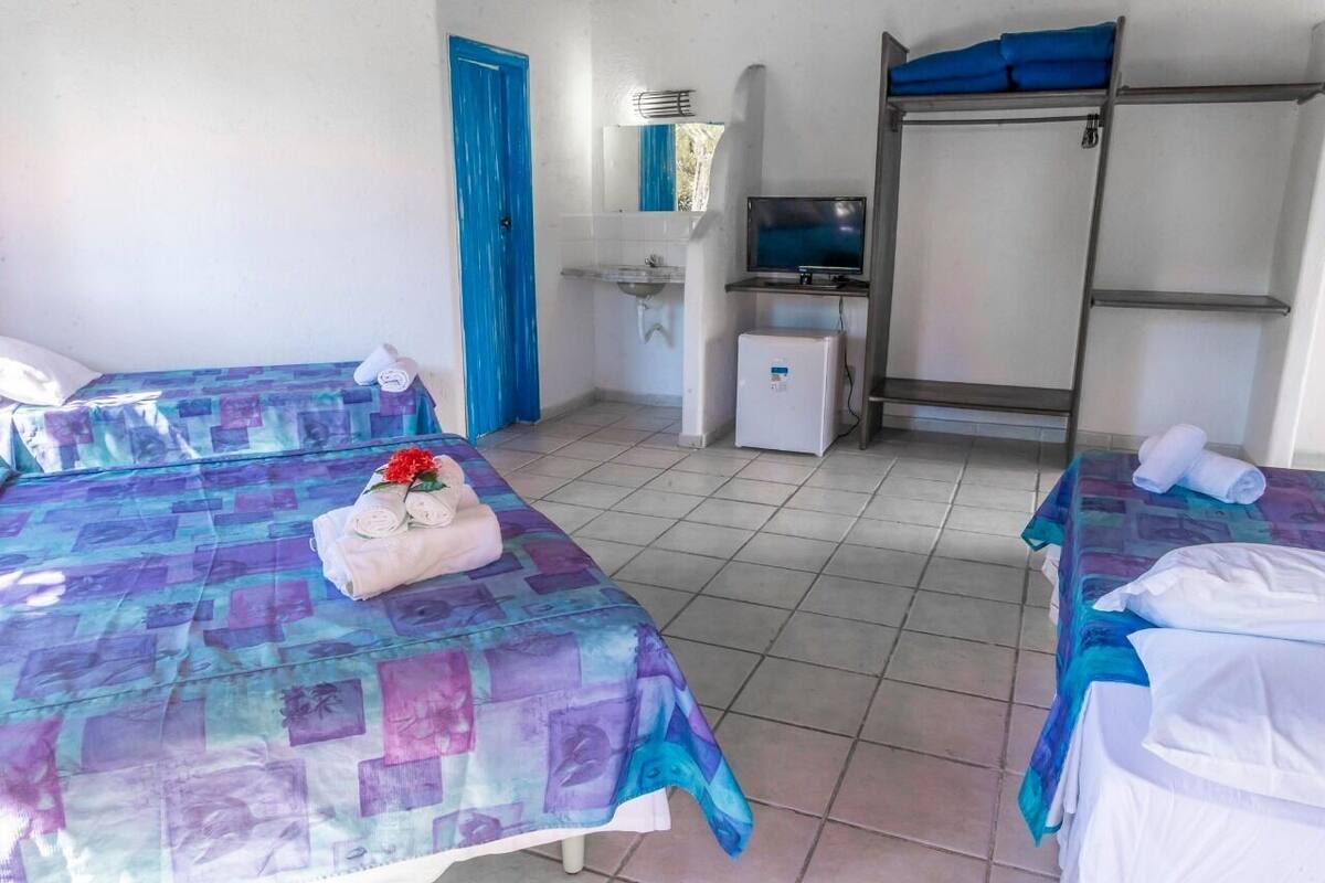A hotel room with two beds, a small TV, a mini-fridge, and a blue door.