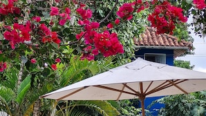 A patio area with a pool, a wooden bench, and an umbrella. - Pousada Varanda do Sol (Porto Seguro)