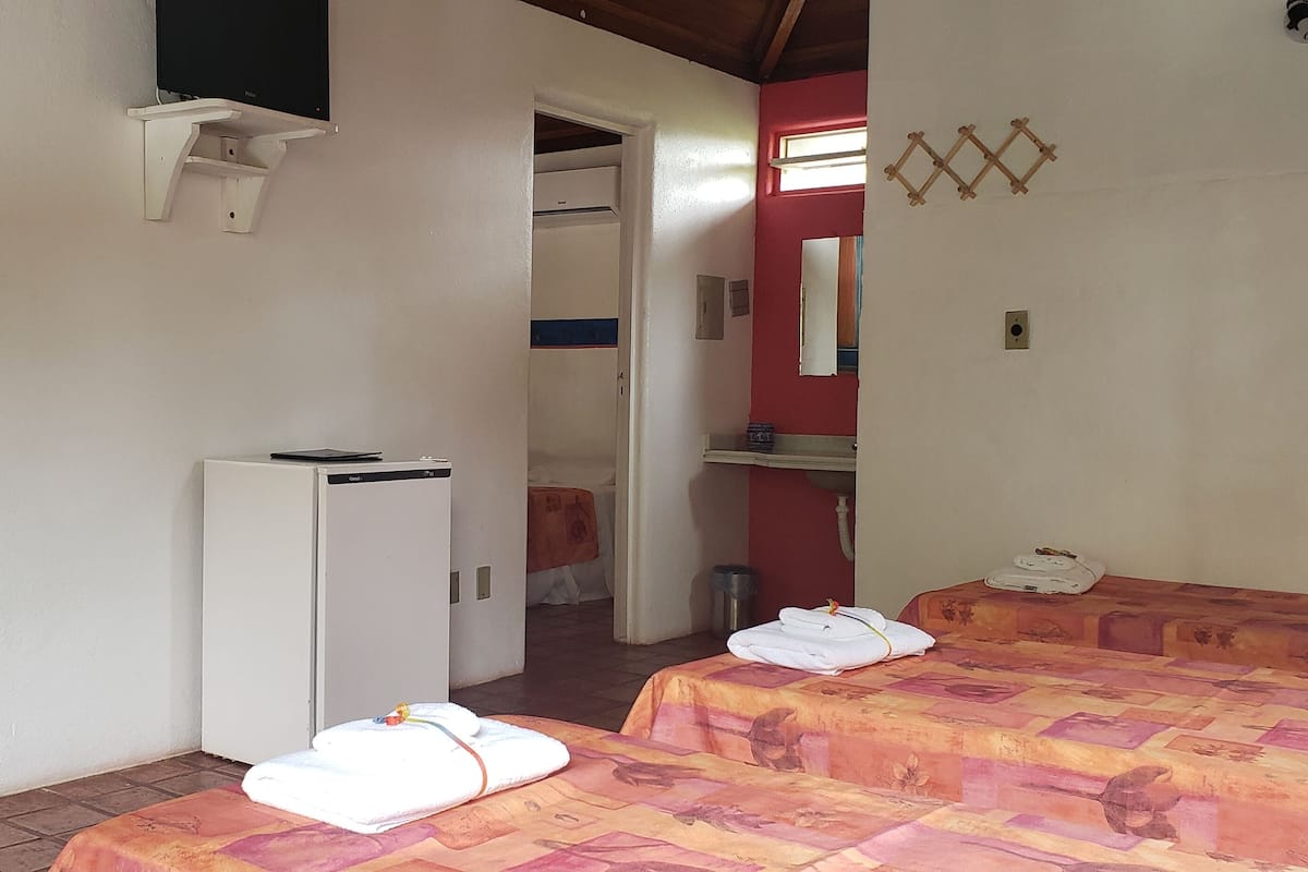 A room with two beds, a small white refrigerator, a wall-mounted TV, and a red wall with a window.