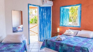 A room with two beds, a mirror, an air conditioner, and a window with a view of greenery. - Pousada Varanda do Sol (Porto Seguro)