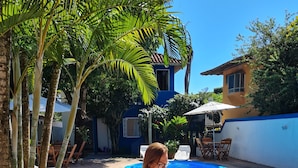 A person sitting at a wooden table by a swimming pool, reading a book. - Pousada Varanda do Sol (Porto Seguro)