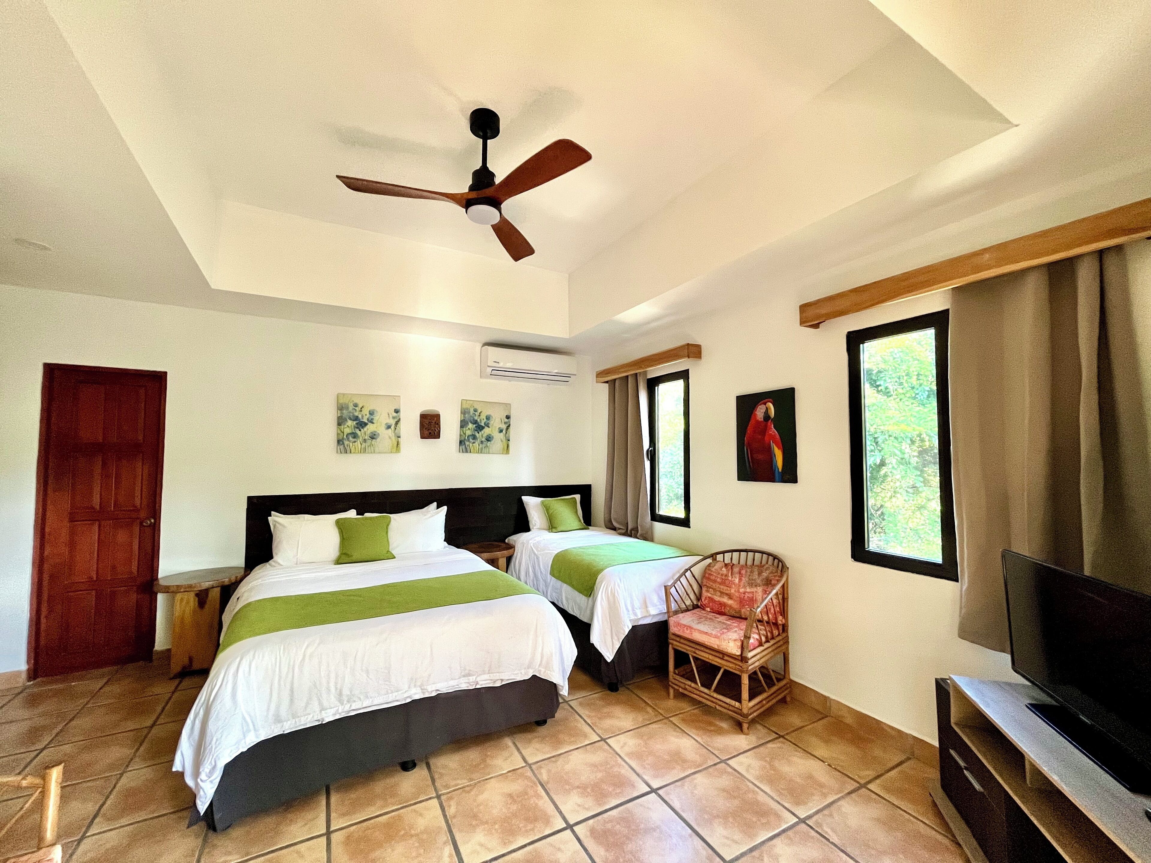 A bedroom with two beds, a ceiling fan, a TV, and artwork on the walls.