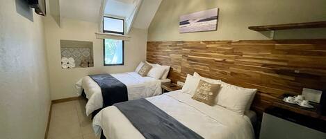 A bedroom with two beds, a wooden headboard, a small window, a TV, and a shelf with cups.