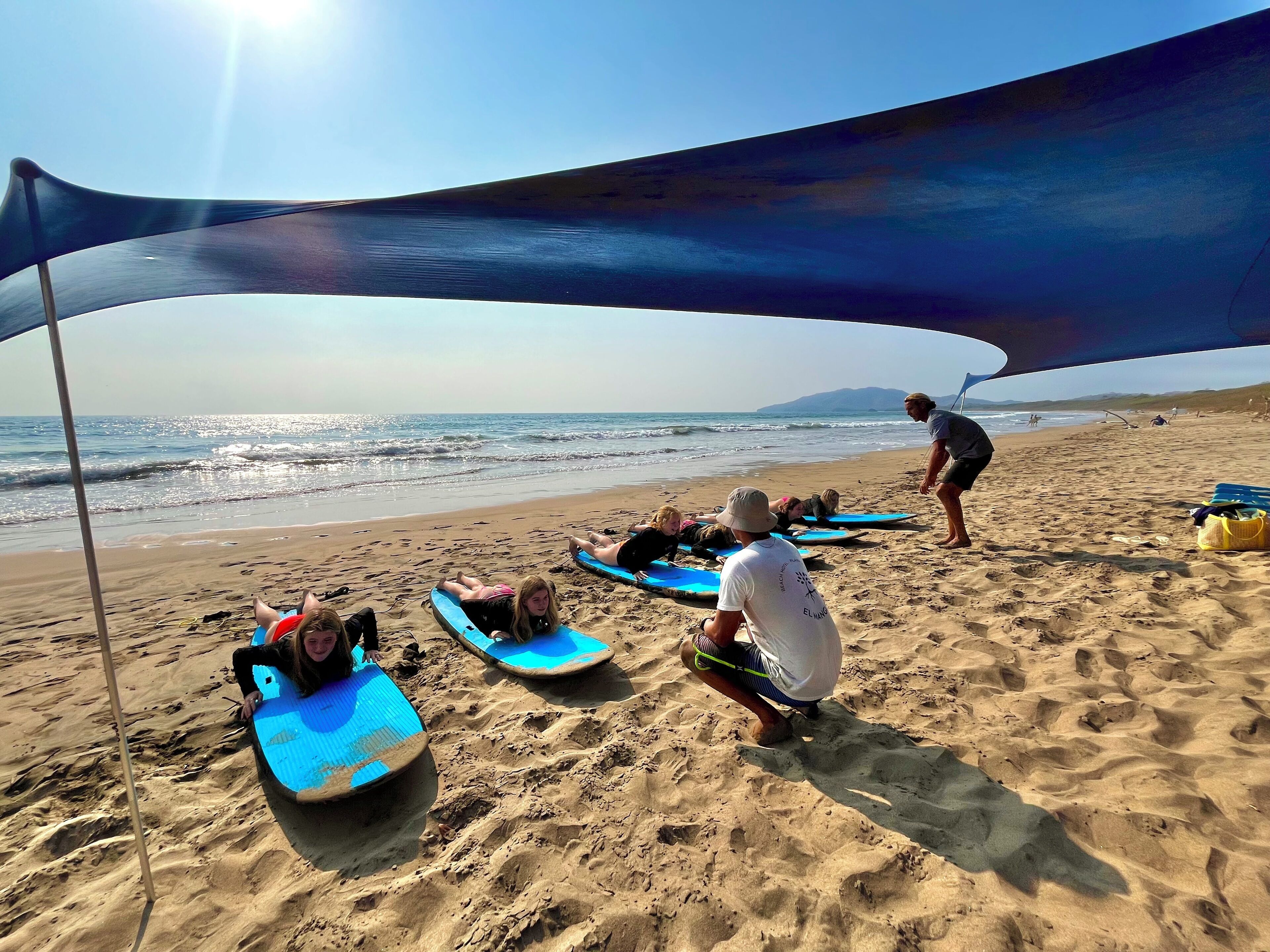 Ein Strand mit Menschen, die auf Surfbrettern unter einem Sonnensegel liegen.