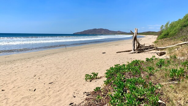 Ein Strand mit blauem Himmel, sandigem Ufer und einem fernen Berg.