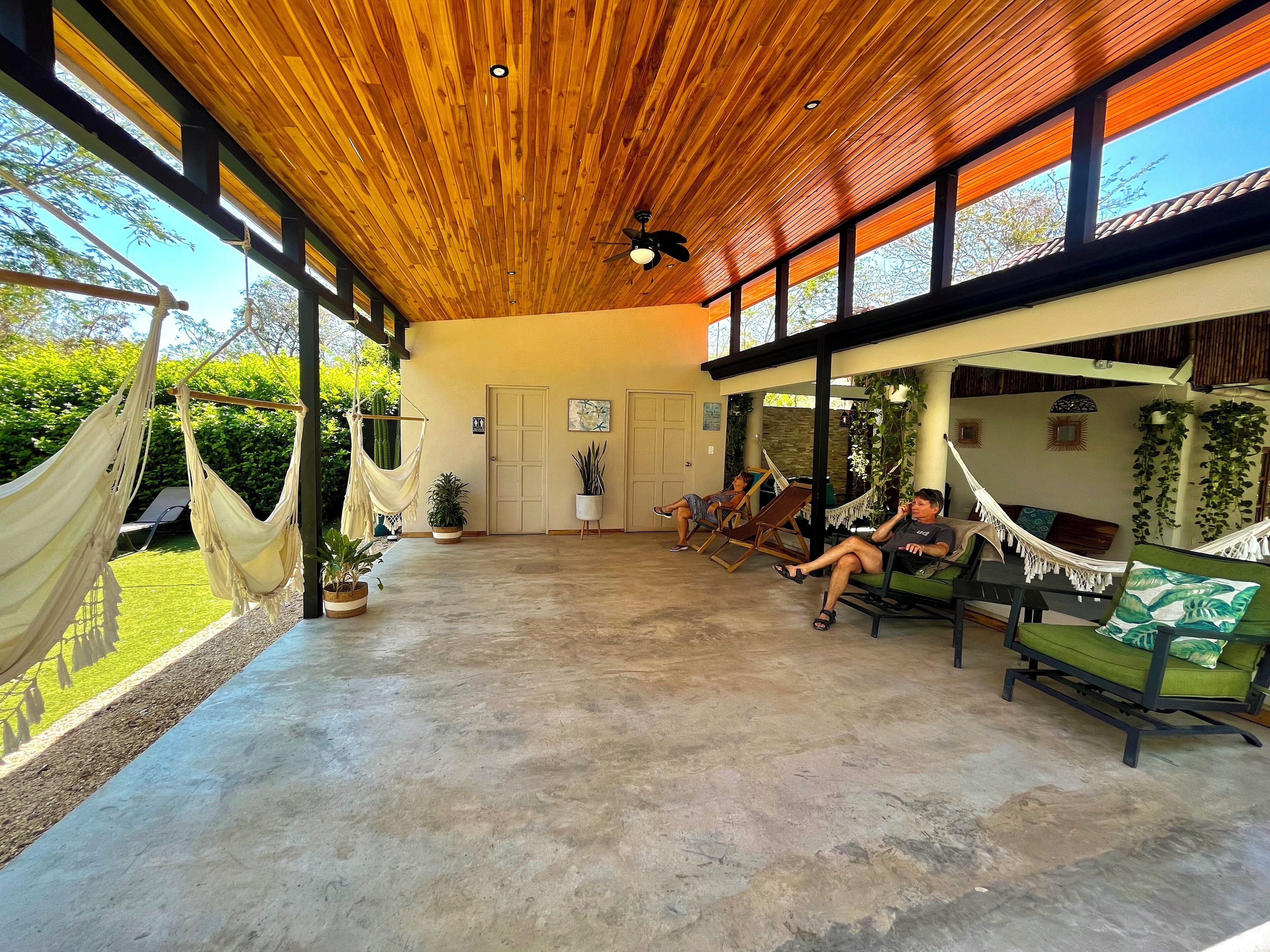 A spacious indoor area with a high ceiling and wooden beams, featuring several hammocks and lounge chairs, suggesting a relaxation area.
