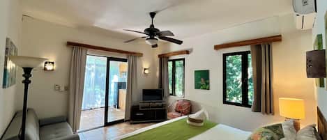 A hotel room with a bed, a chair, a ceiling fan, a television, and a view of the outdoors.