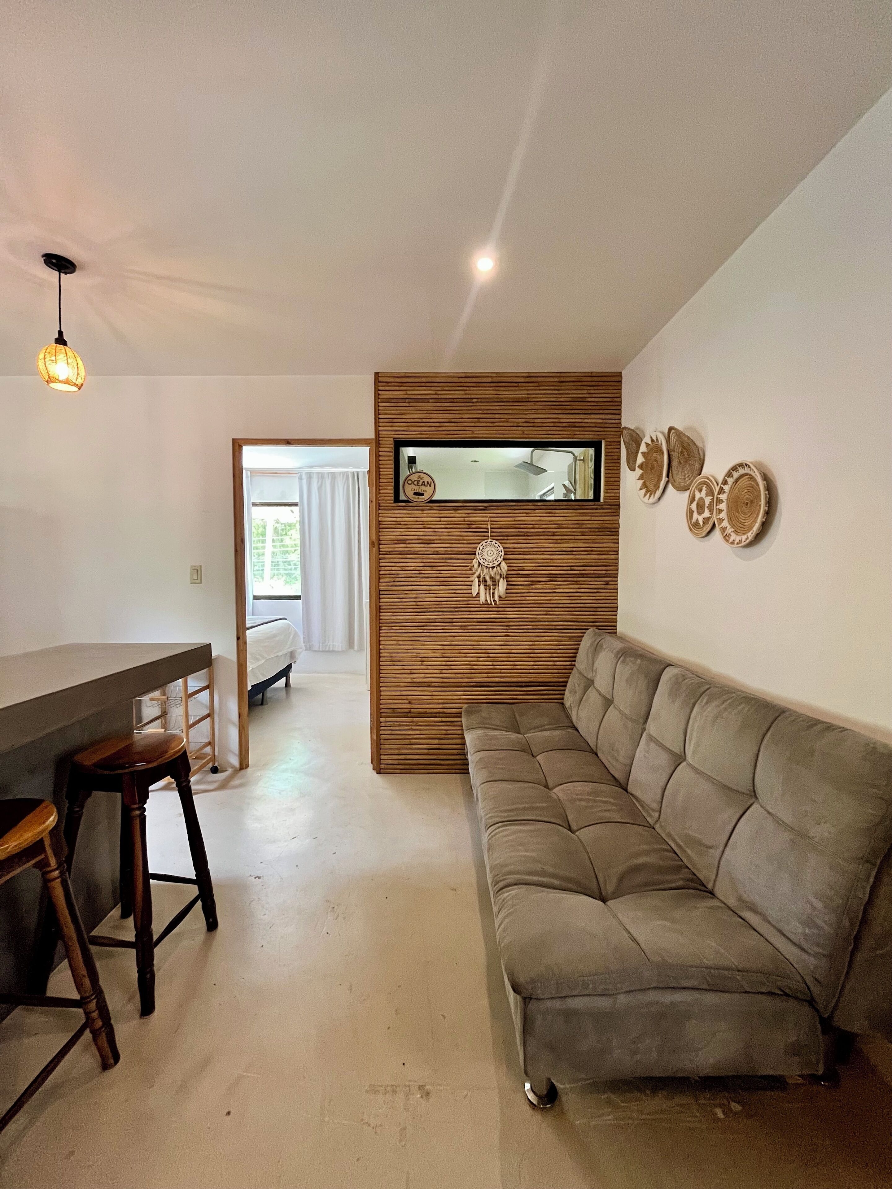 A modern living room with a sofa, a dining area with stools, a wooden accent wall, and a mirror.
