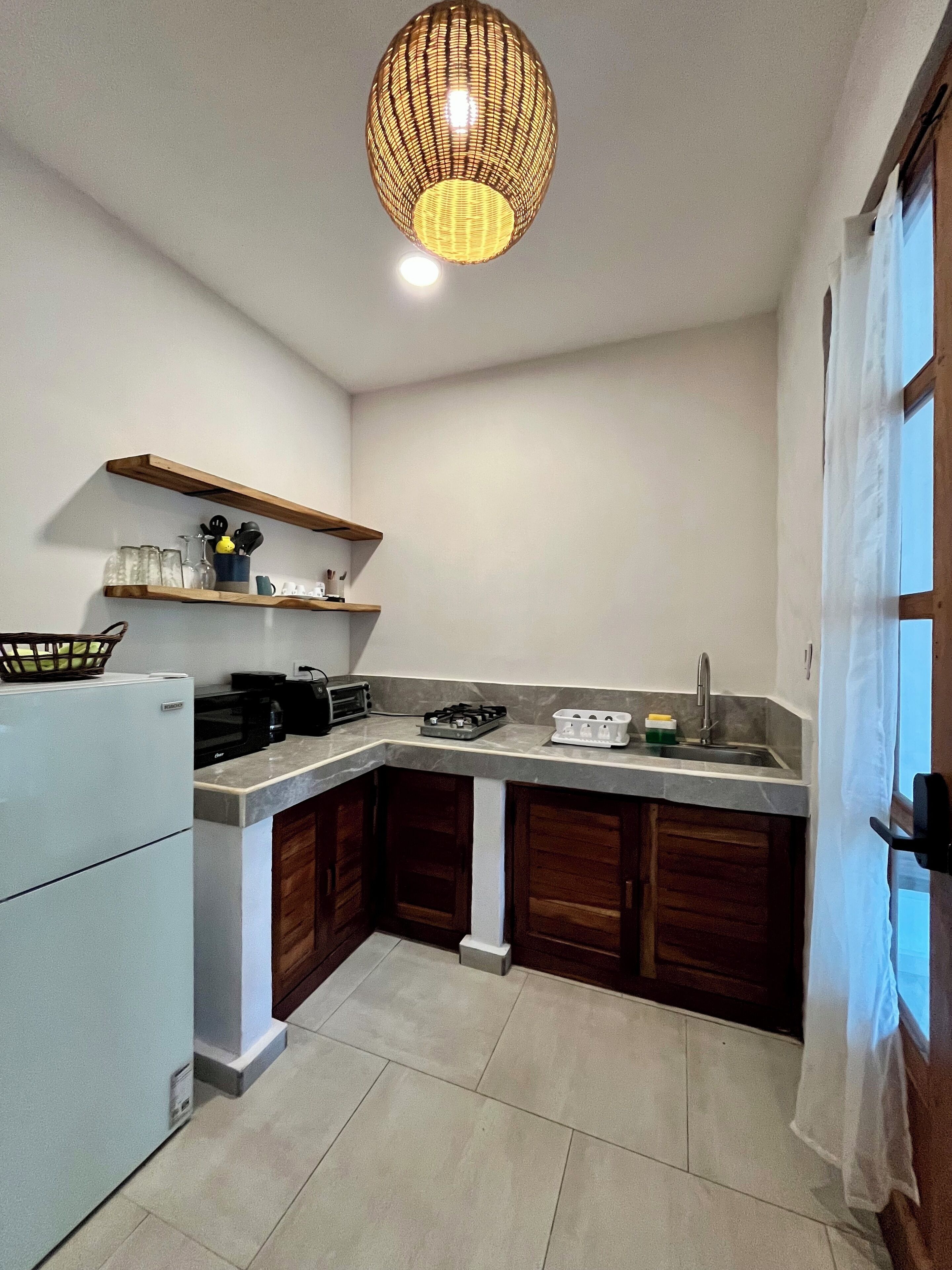 A compact kitchen with a built-in gas stove, a microwave, and a sink. There are wooden cabinets and a hanging light fixture.