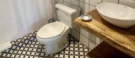 Une salle de bain comprenant des toilettes, un lavabo, une étagère en bois avec des serviettes et un miroir.