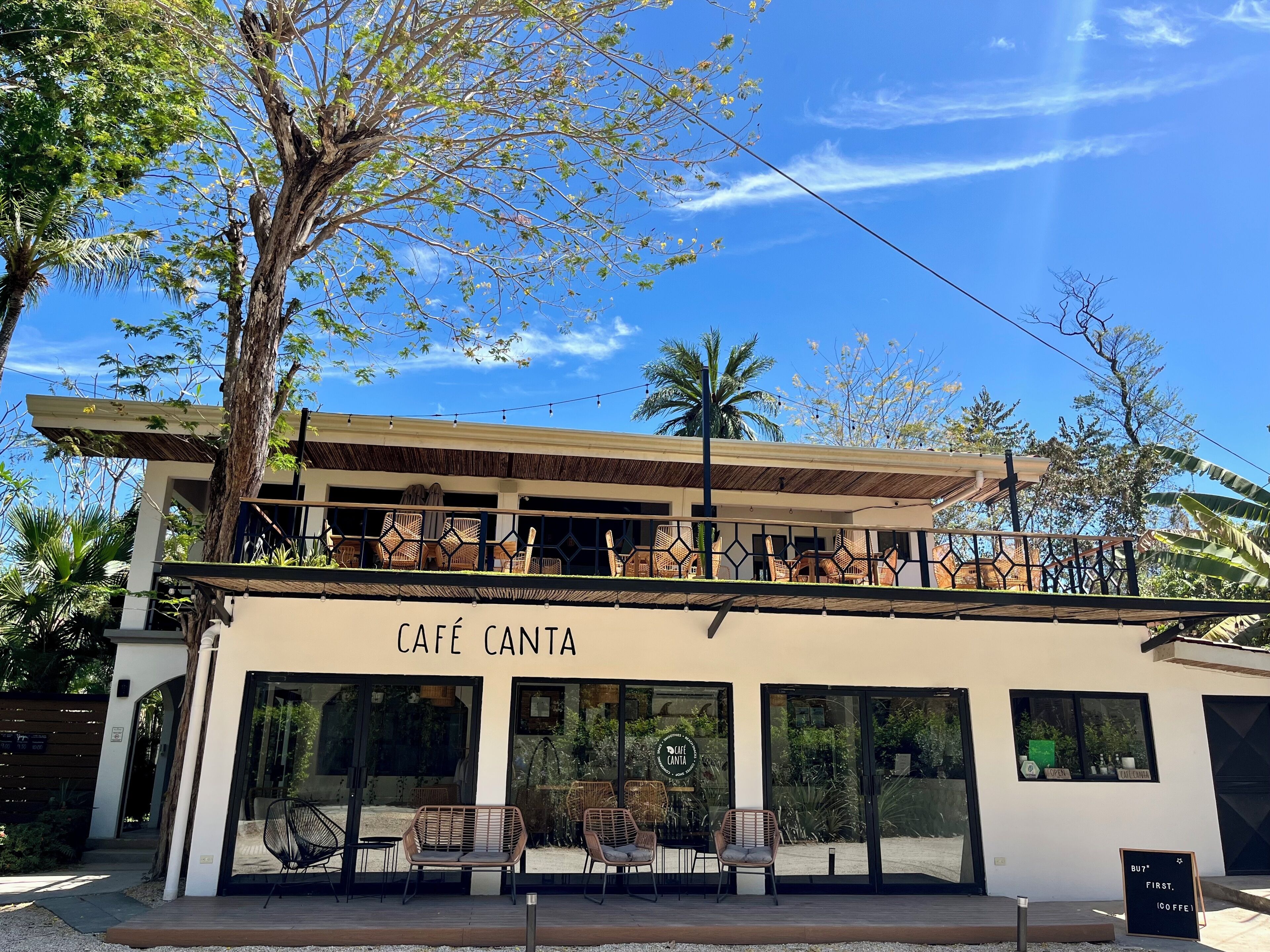 Un café con terraza, un cartel que dice "CAFE CANTA" y vistas de la vegetación circundante.