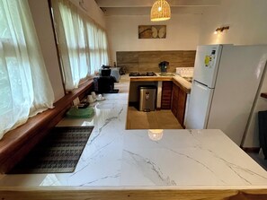 A kitchen with a marble countertop, wooden cabinets, a stainless steel refrigerator, and a small sink.