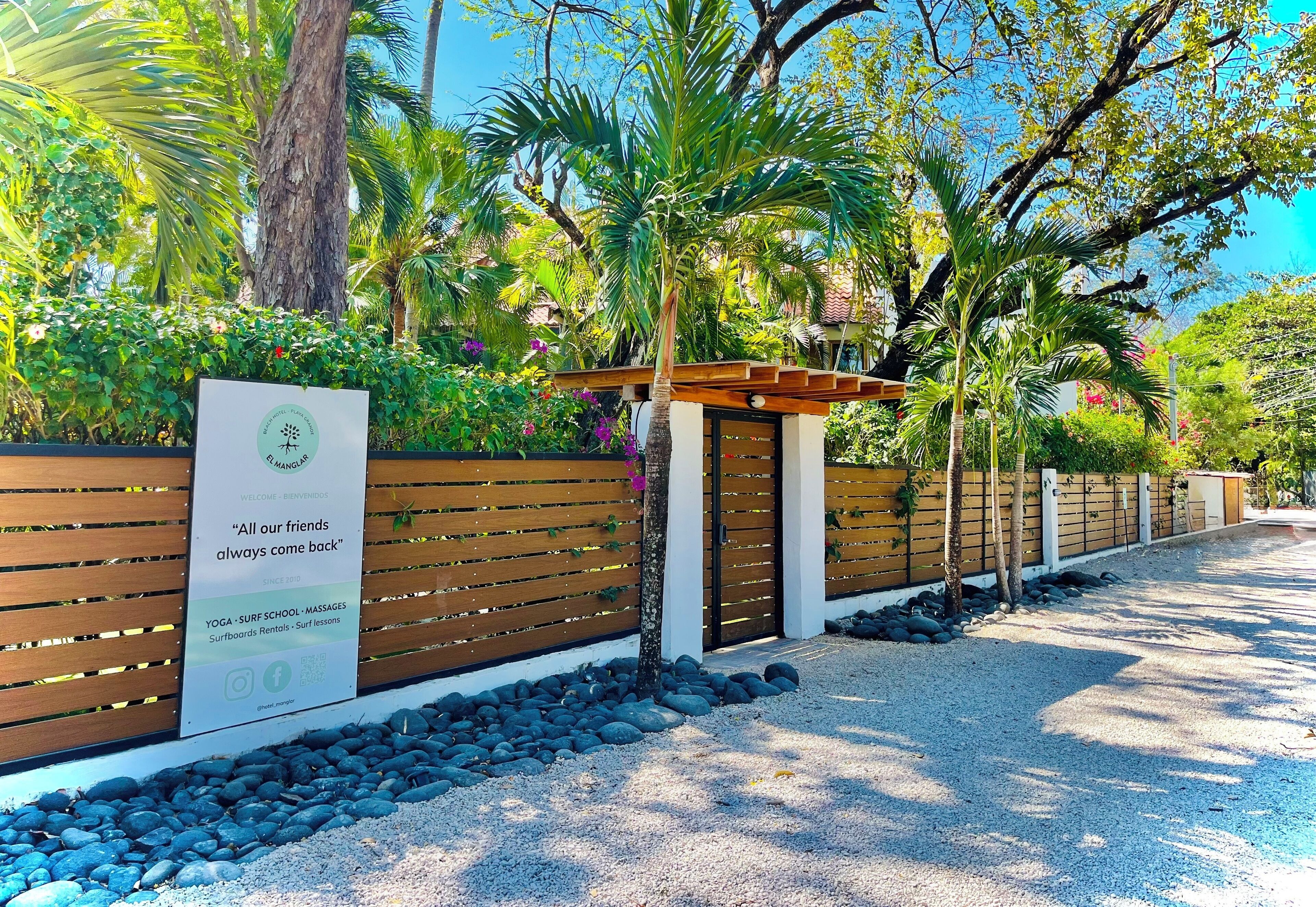 A wooden fence with a signboard advertising yoga, surf school, massages, and surfboards rentals.