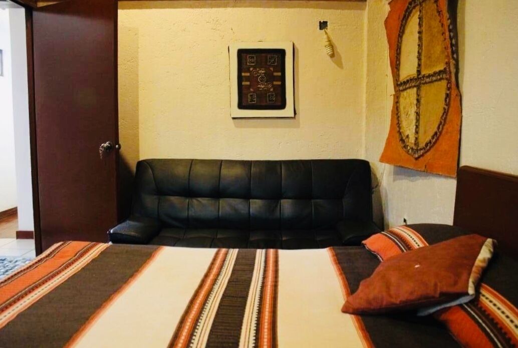 A room with a black leather sofa, a bed with striped bedding, a framed picture on the wall, and a tapestry.