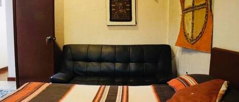 A room with a black leather sofa, a bed with striped bedding, a framed picture on the wall, and a tapestry.