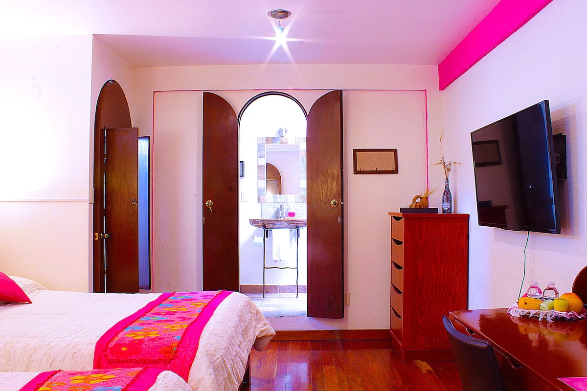 Une chambre d’hôtel comprenant un lit, une commode en bois, un téléviseur et un bureau avec une chaise.