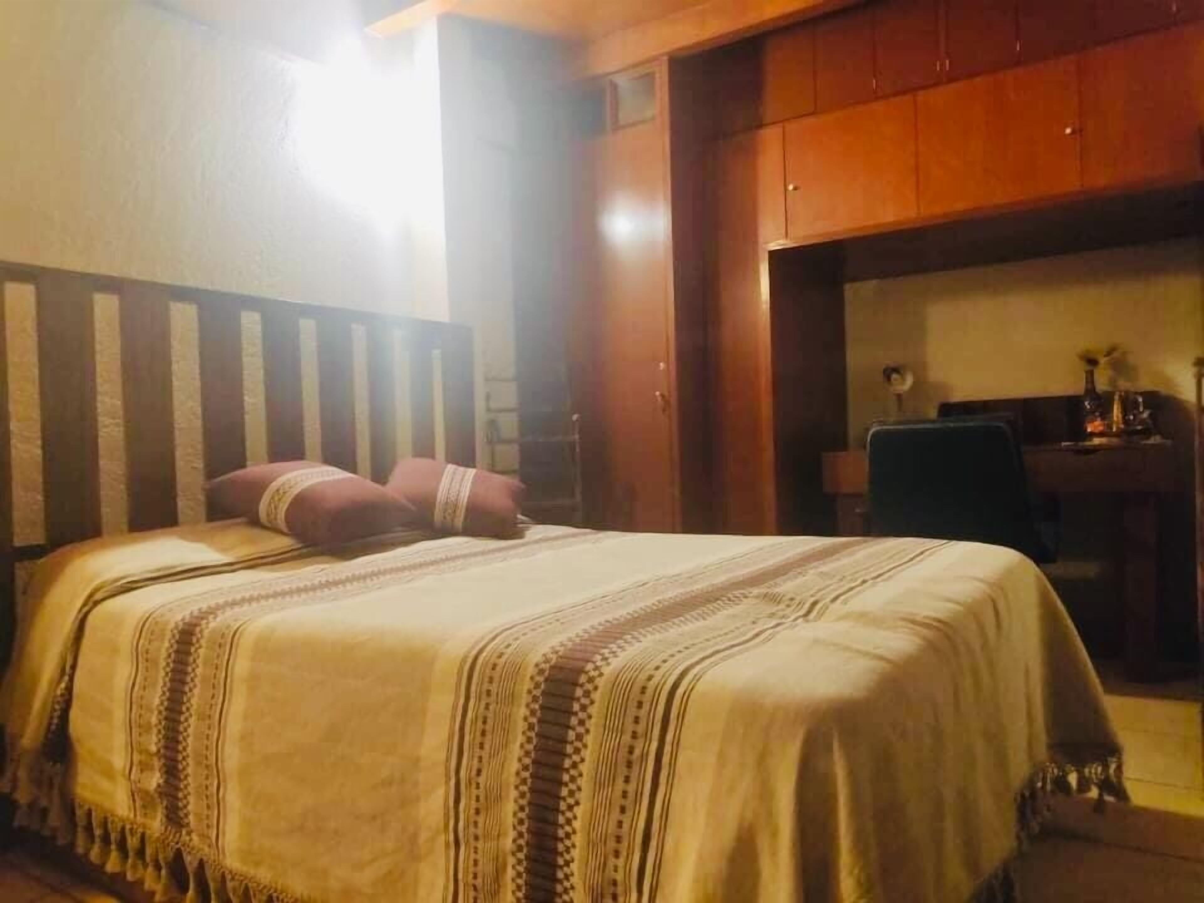 Ein Schlafzimmer mit Bett, Holz-Kopfteil und Schreibtisch mit Stuhl.
