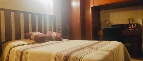 Ein Schlafzimmer mit Bett, Holz-Kopfteil und Schreibtisch mit Stuhl.