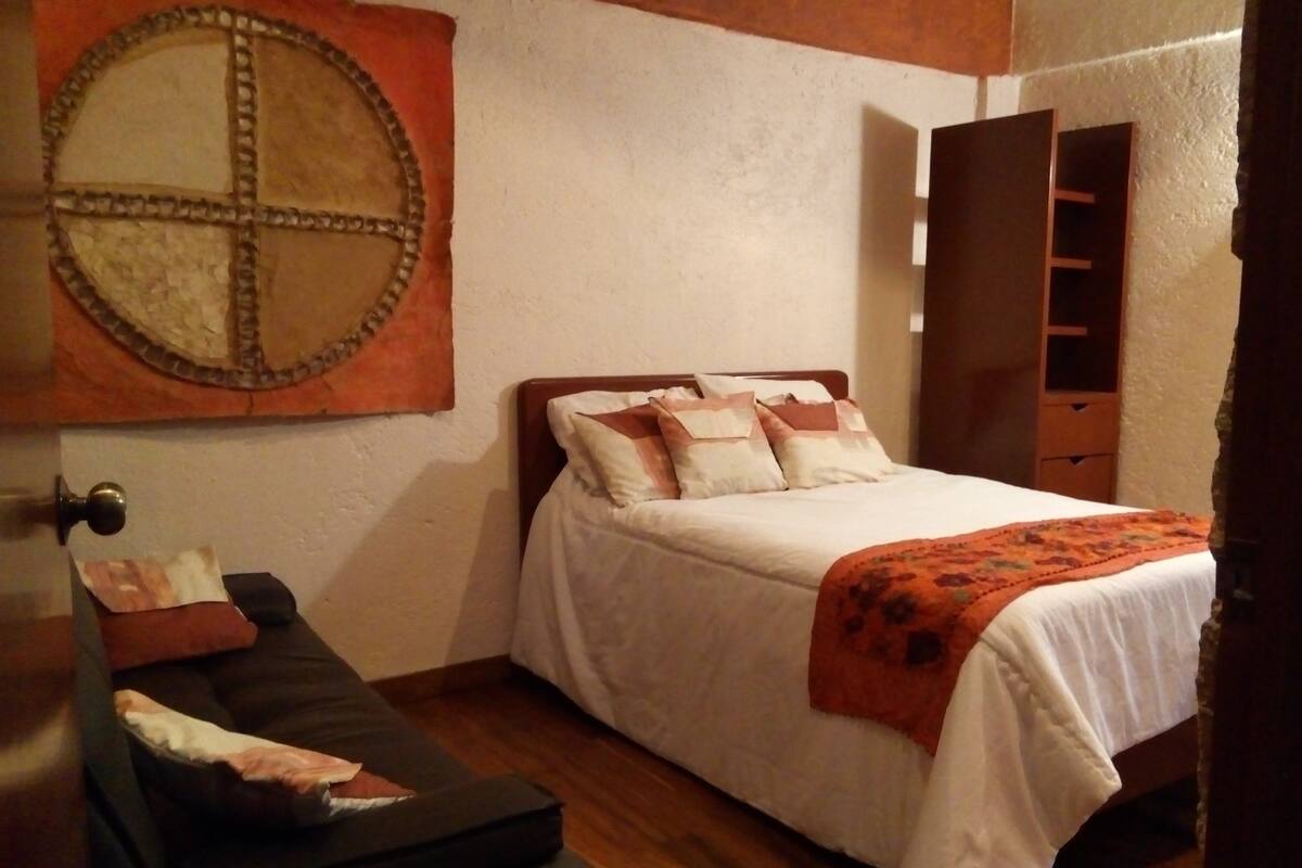 Une chambre à coucher comprenant un lit, une tête de lit en bois, un miroir rond fixé au mur et une armoire en bois.