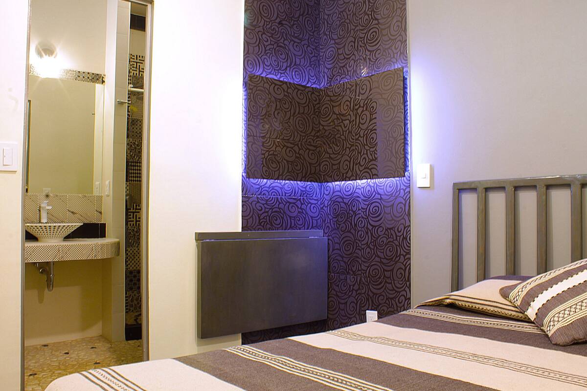 Une chambre à coucher comprenant un lit, une table de chevet, un téléviseur fixé au mur et un mur décoré d’un motif.