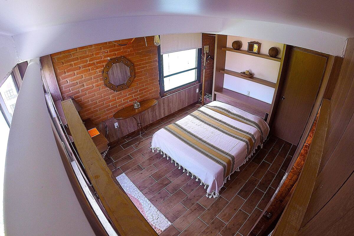 Une chambre avec un mur en briques, un cadre de lit en bois et une fenêtre.
