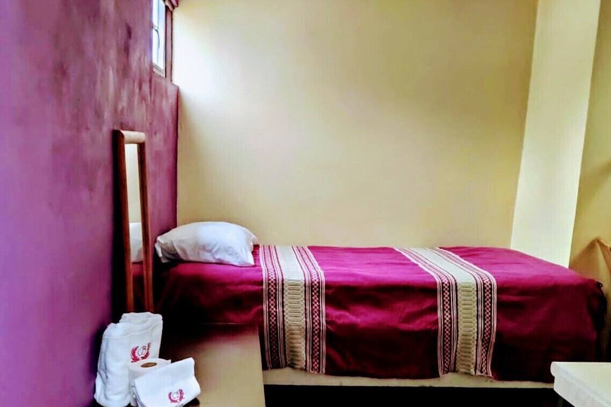 Une petite chambre avec un lit simple, un banc en bois, une petite table et une fenêtre.