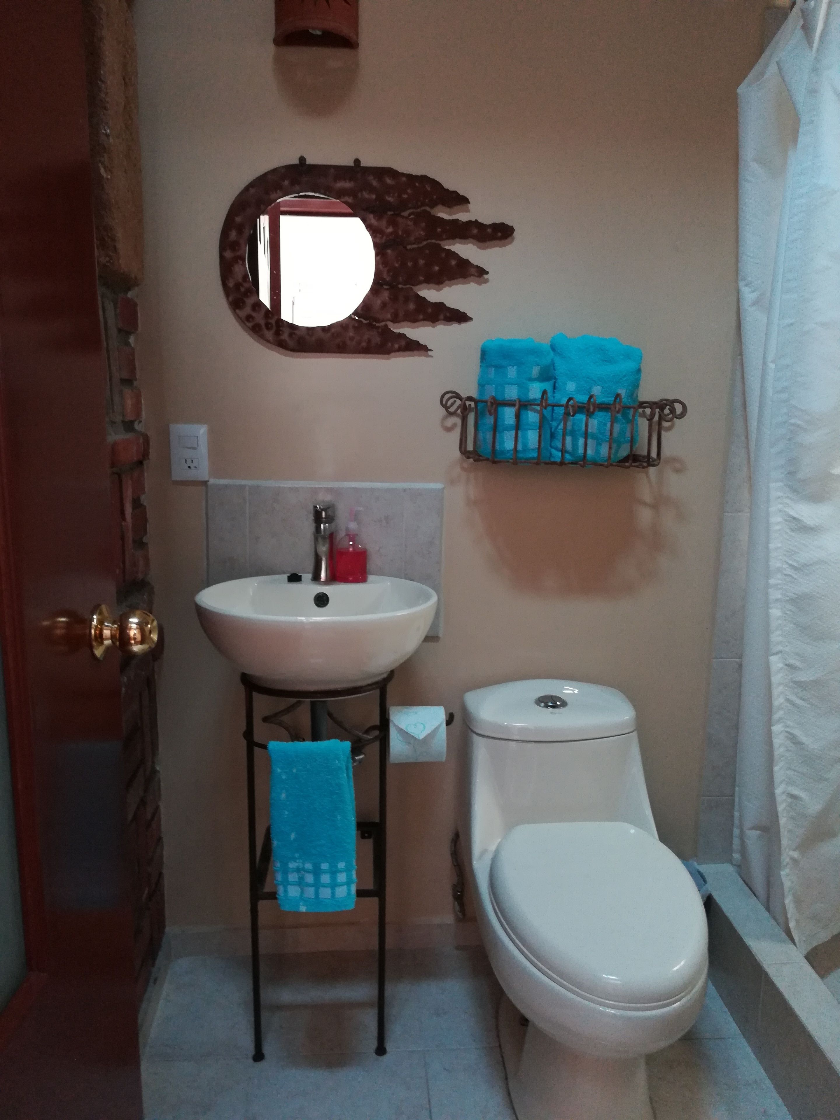Une salle de bain avec un lavabo blanc, des toilettes, un miroir avec un cadre décoratif et un porte-serviettes avec des serviettes bleues.