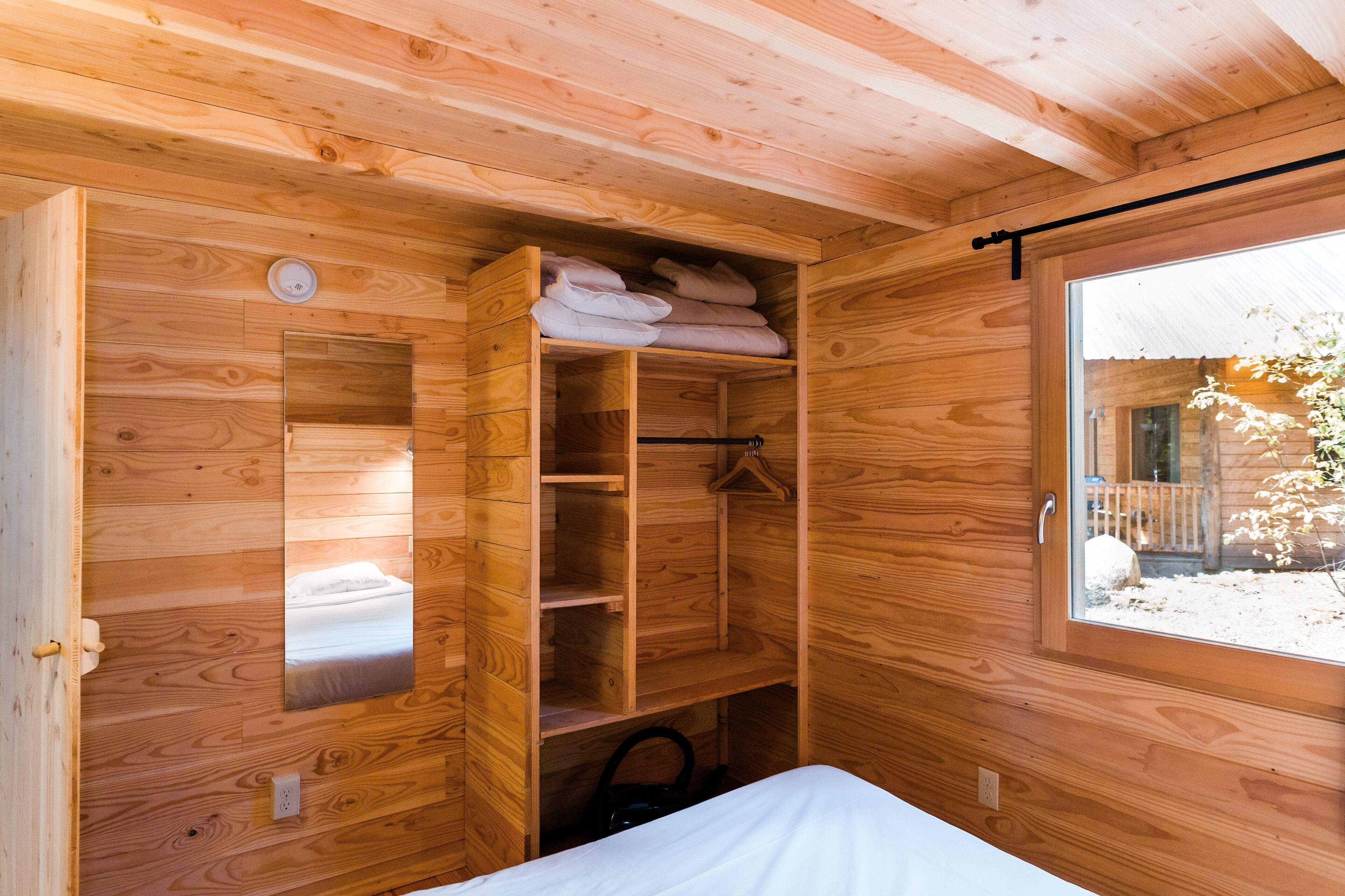 Une chambre dans un chalet en bois, avec un lit, une armoire intégrée et une fenêtre.