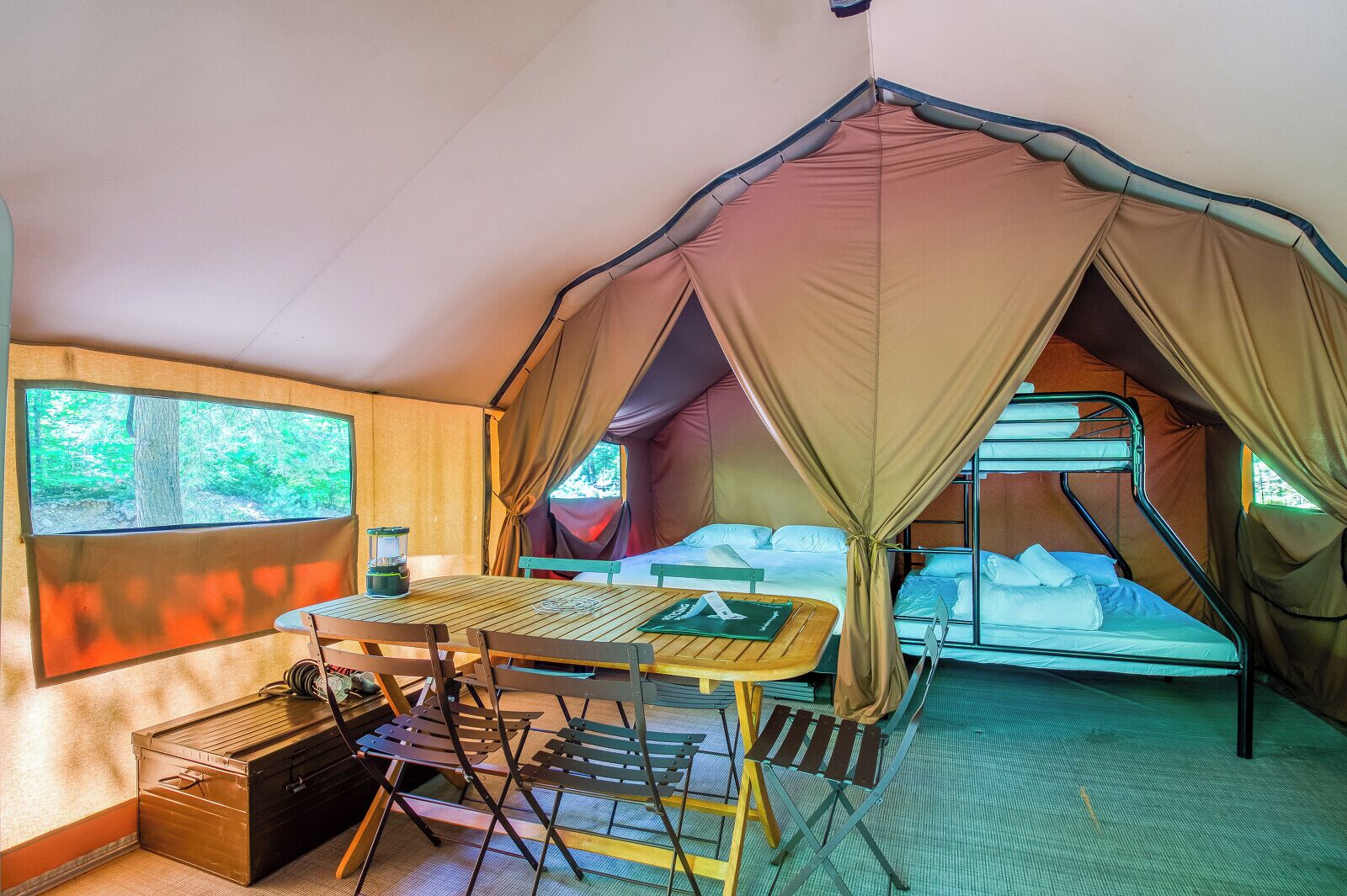 A tented room with a bunk bed, a table, and a chair.