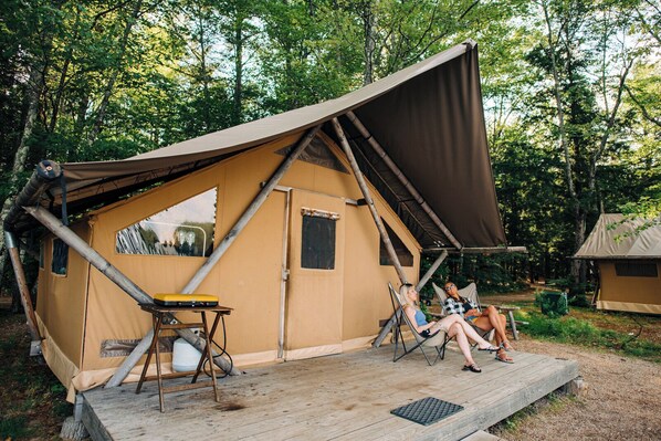 A tent with a wooden deck, two reclining chairs, and a table. - Huttopia White Mountains (Conway)