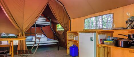 Une tente compacte et bien équipée, dotée de lits superposés, d’une petite kitchenette et d’une fenêtre donnant sur une forêt.