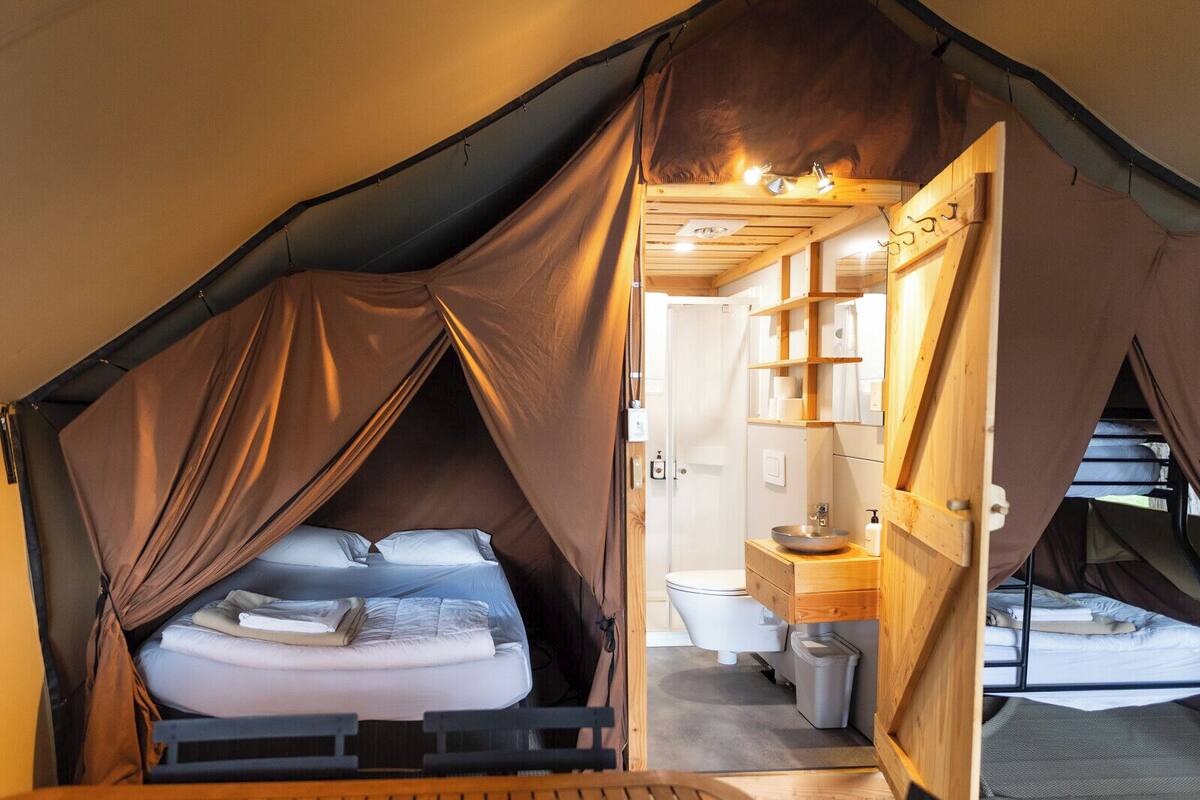 A tent with a bed, a small bathroom with a sink and toilet, and a mirror.