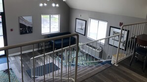 A spacious room with a high ceiling, a modern chandelier, a staircase with a railing, and a view of a parking area through the windows. - DuPont Suites (Louisville)