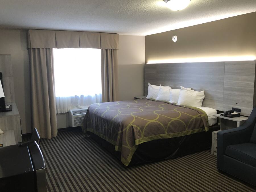 Habitación de hotel con cama, escritorio, silla, mesita de noche, lámpara y ventana con cortinas.