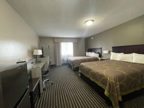 A hotel room with two beds, a desk, a chair, a TV, and a window with curtains.