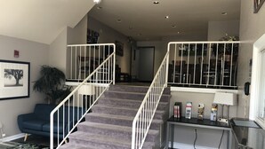 A staircase with white railings leading to a second floor. There is a blue sofa and a table with magazines and a lamp on the landing. - DuPont Suites (Louisville)