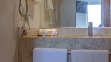 Un baño con encimera de mármol, lavamanos, espejo y perchero.