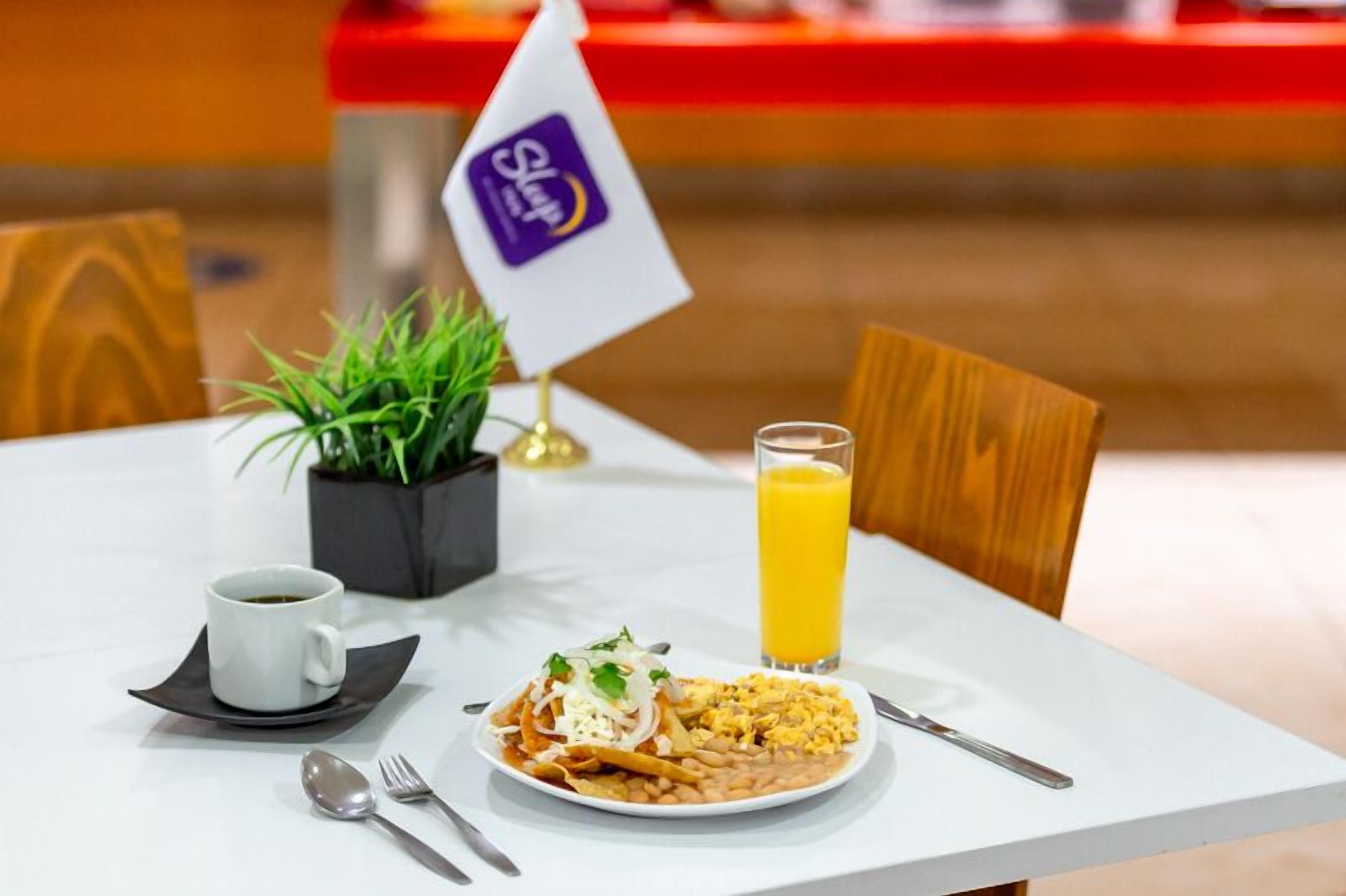 Een eettafel met een bord eten, een glas sinaasappelsap, een kop koffie en een kleine plant.