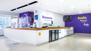 Una zona de recepción con un cartel de 'Welcome', un reloj y un televisor montado en la pared.