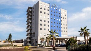 Un hotel Sleep Inn de varios pisos con fachada azul y blanca, rodeado de palmeras y un estacionamiento.
