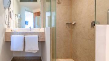 Un baño moderno con ducha de vidrio, lavabo con espejo y dos toallas colgadas en un perchero.