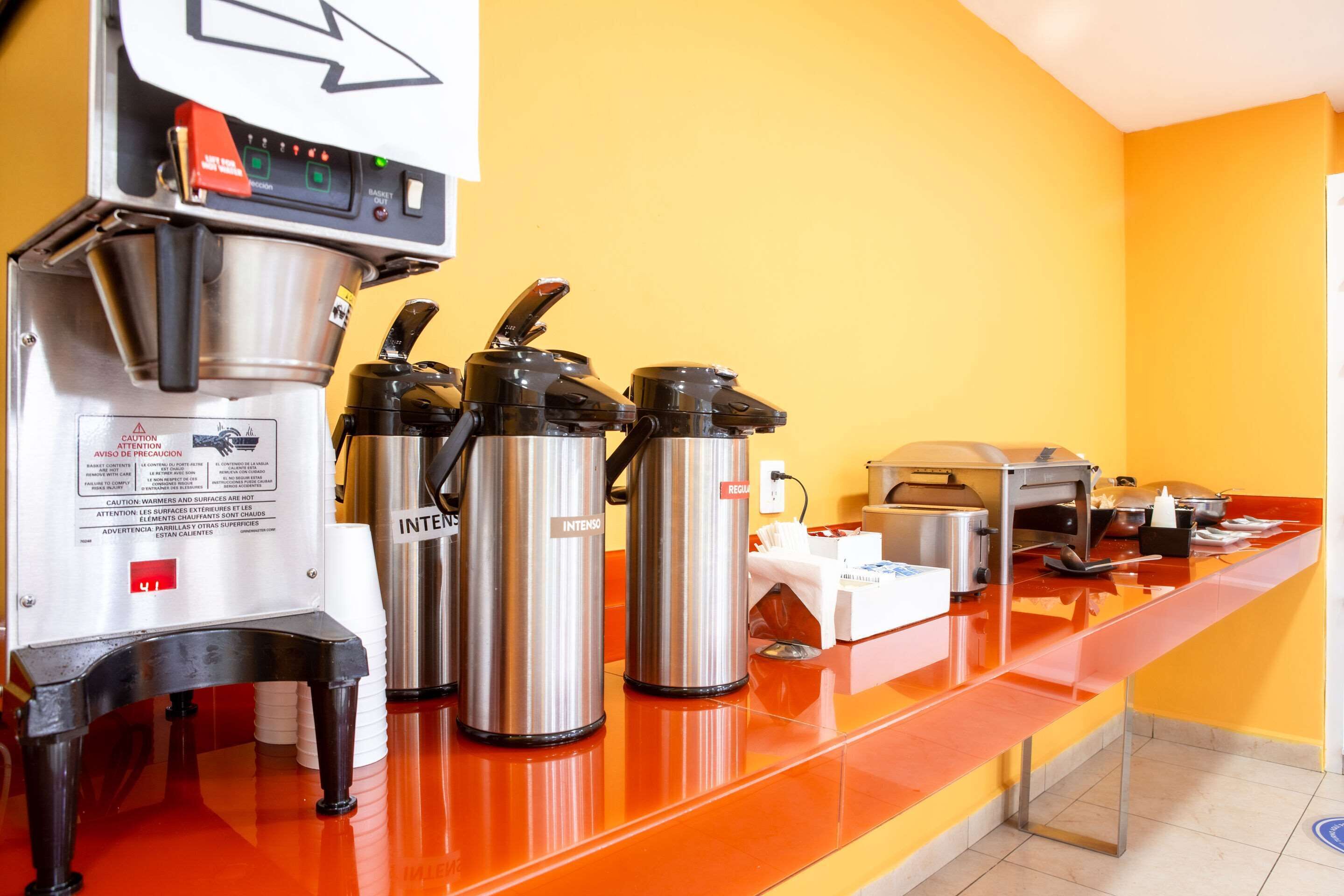 A coffee station with a coffee machine, two Intenso insulated coffee carafes, and a toaster on a red counter.