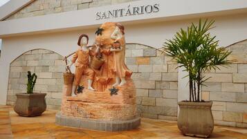 A stone wall with the sign 'SANITÁRIOS' and a sculpture of two figures with baskets.