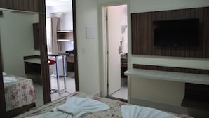 A hotel room with a bed, a TV mounted on the wall, a bathroom with a shower, and a small table with a chair.