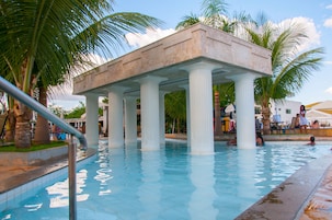 Piscina com estrutura arquitetônica clássica, palmeiras e céu claro.