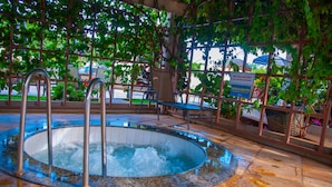 A hot tub with metal railings and a tiled floor, surrounded by greenery and a sign in a foreign language.