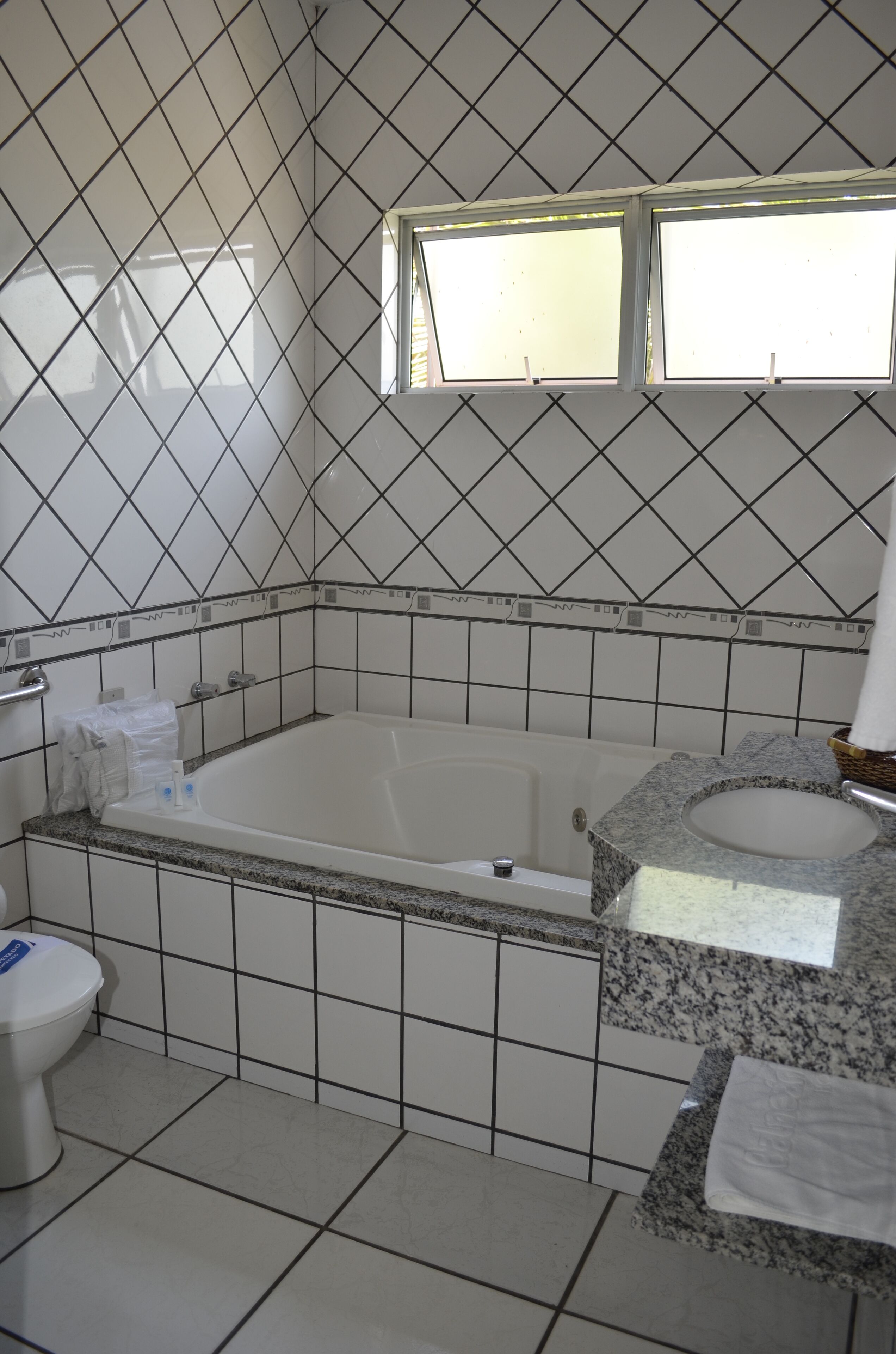 A bathroom with a white tiled wall, a bathtub, a sink, and a window above the sink.