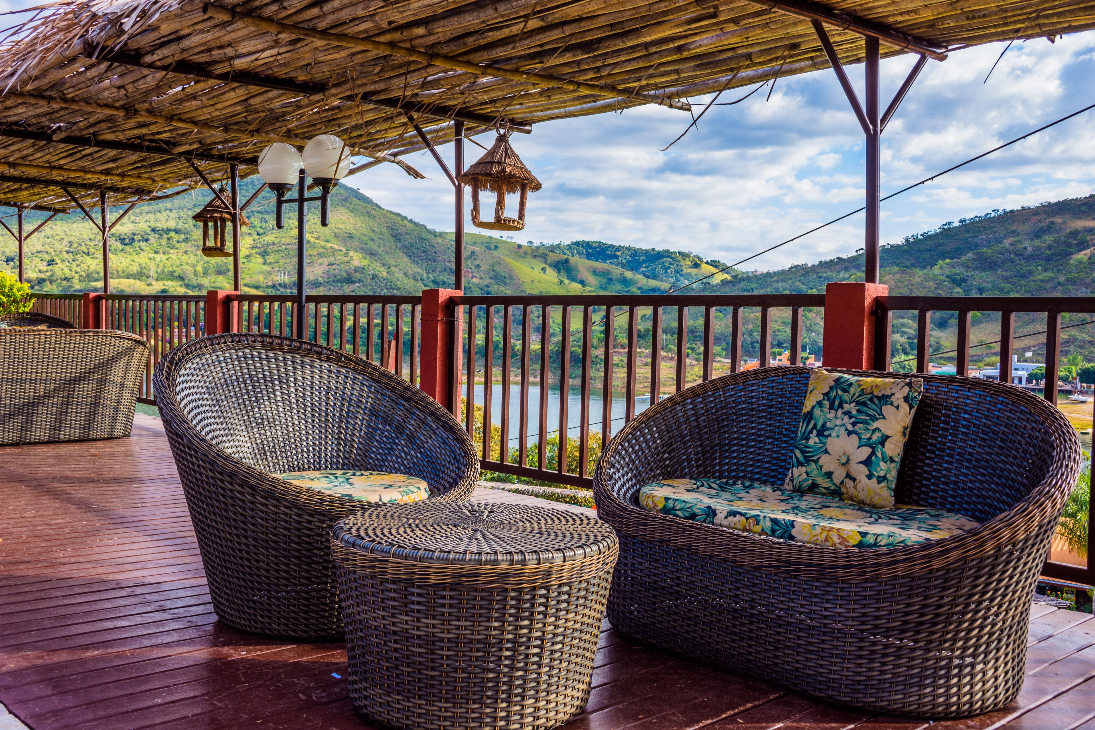 A covered outdoor seating area with wicker furniture and a view of a lake and hills.