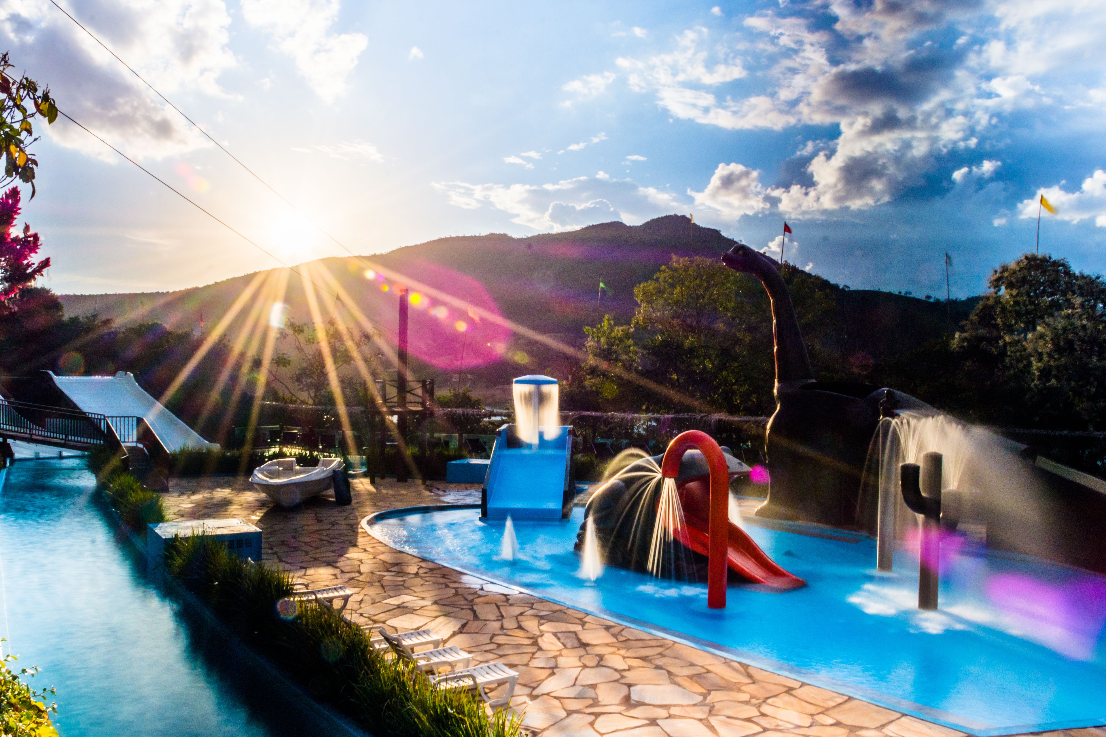 Una piscina con tobogán, fuentes de agua y montañas al fondo.