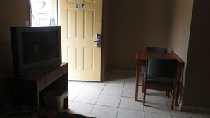 A room with a television on a wooden stand, a dining table with chairs, and a door marked with the number 117.